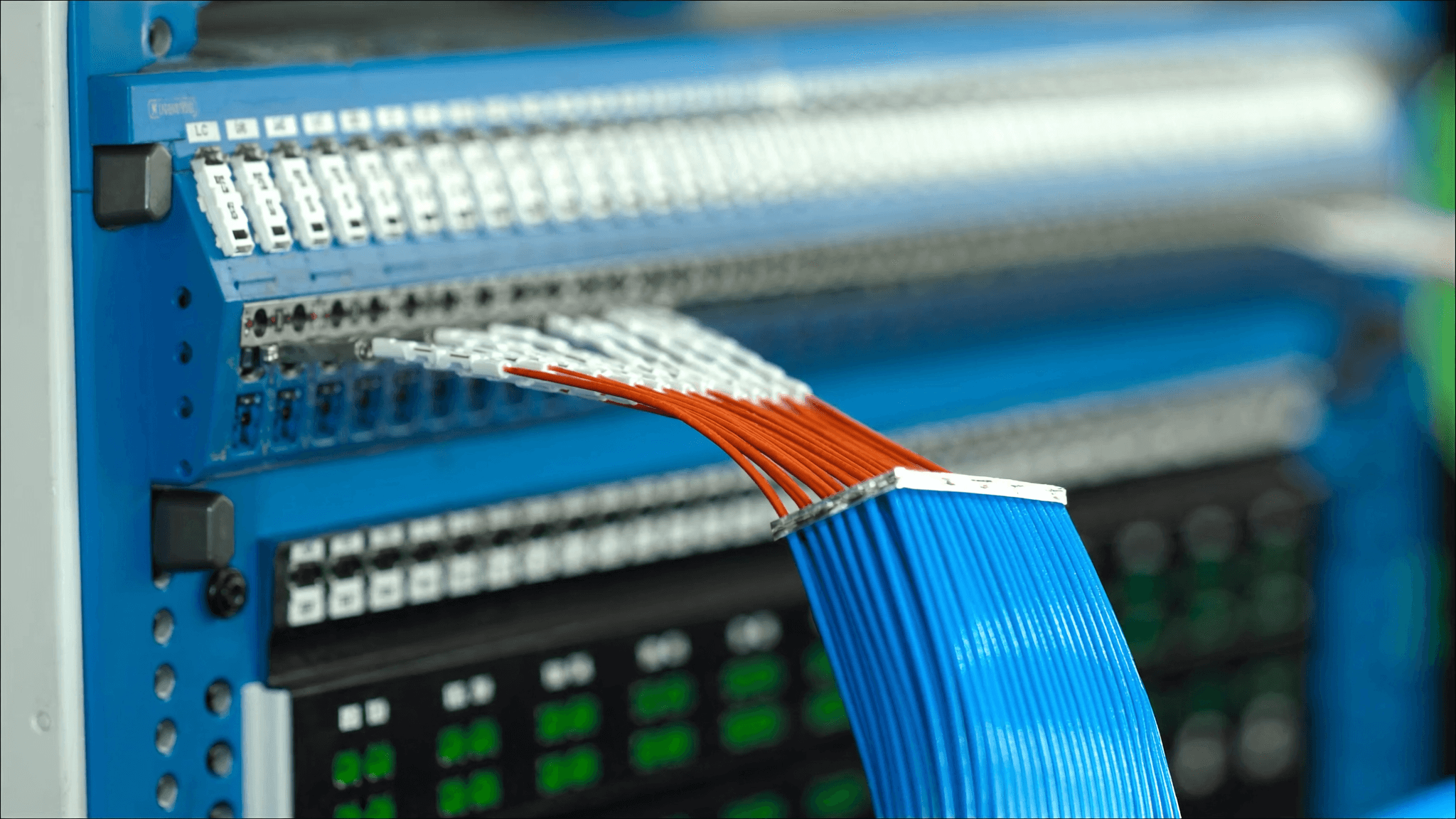 Multiple LC fibre connectors plugged into a high-density blue and orange fibre patch panel with cables fanning out