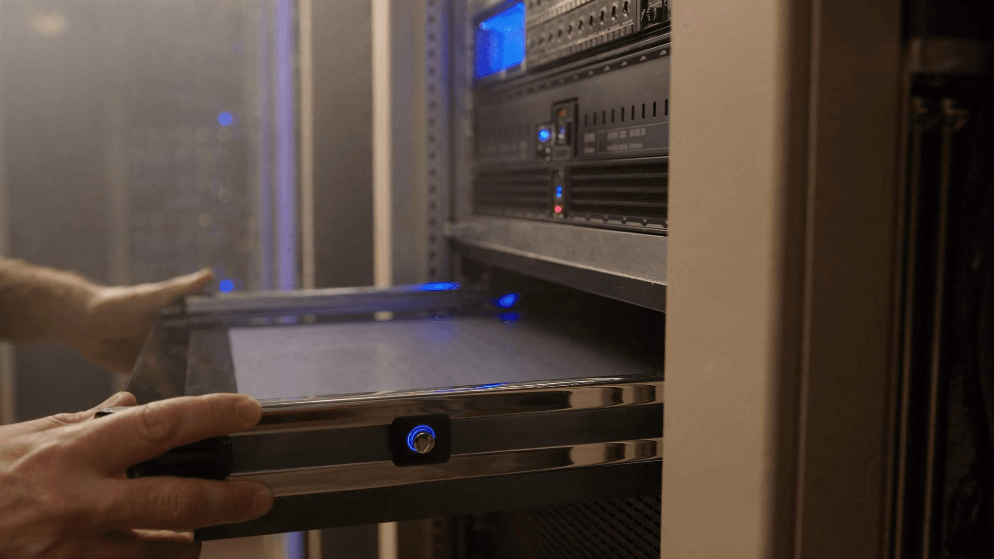 An open server cabinet in a data centre with an engineer sliding a 1U server onto its rack rails, blue LED accent lighting